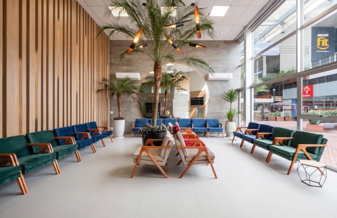 Sala de espera do edifício onde ficam os consultórios, em Osasco, com poltronas, plantas e luz natural.