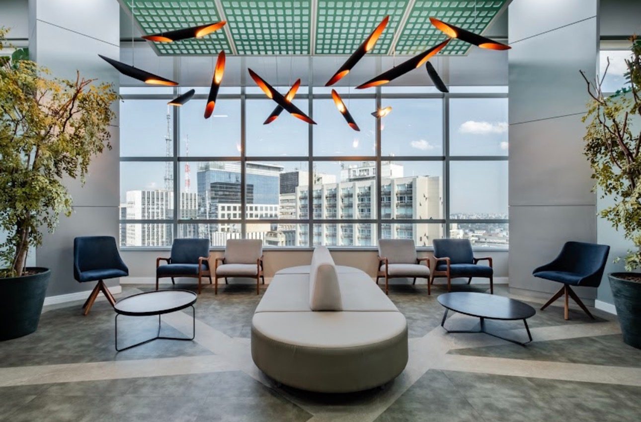 Sala de espera do edifício onde ficam os consultórios, na Avenida Paulista, com poltronas e vista para a cidade.