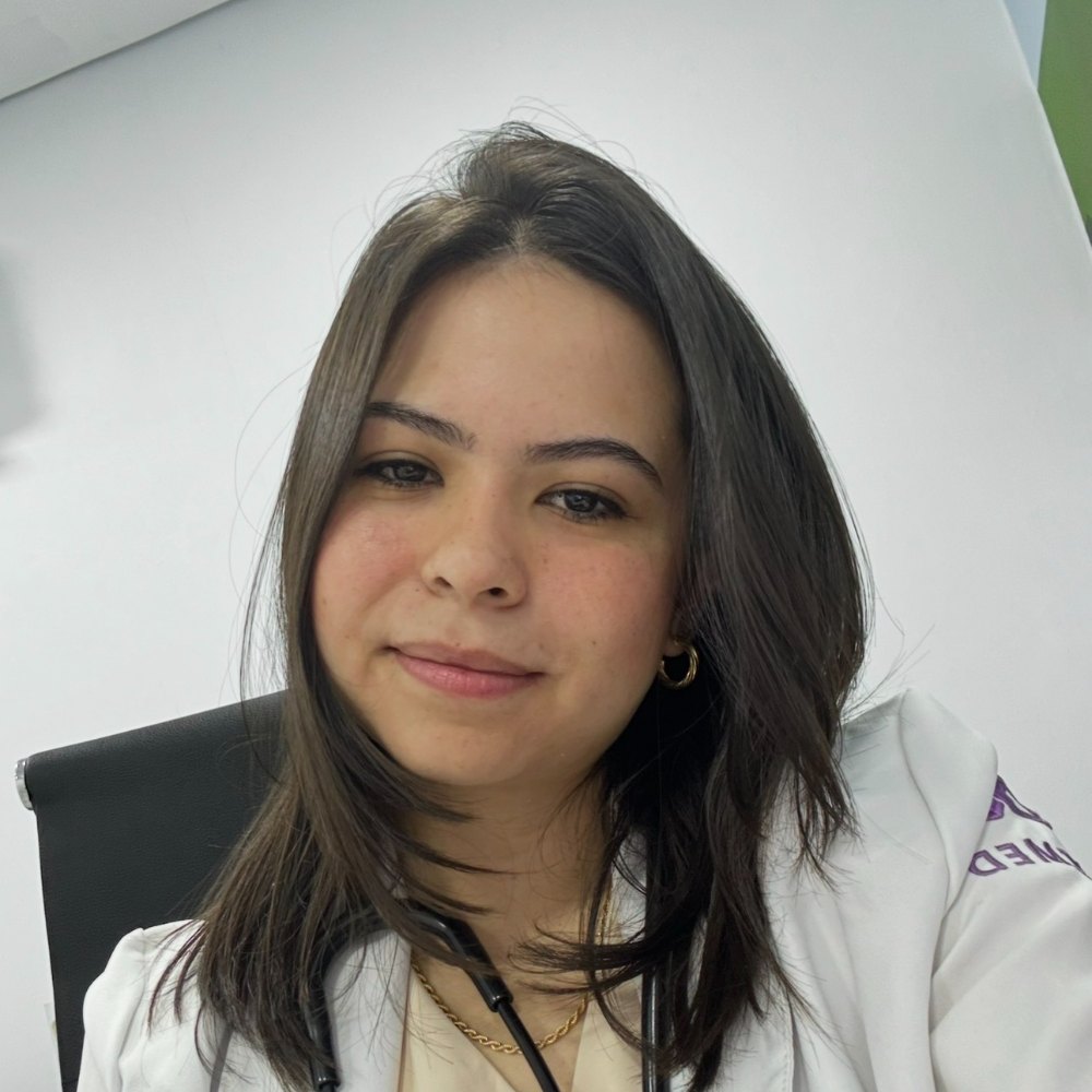 Dra. Taís Fernanda, de jaleco branco e estetoscópio, sentada no consultório.
